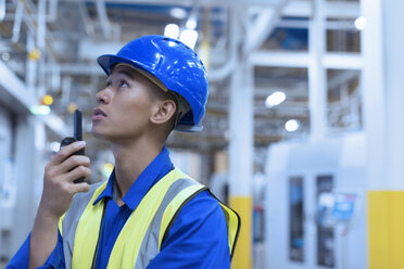 Arbeiter mit Schutzhelm benutzt Walkie-Talkie in einer Fabrik - CAIF09085