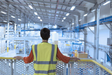 Arbeiter in reflektierender Kleidung auf einer Plattform mit Blick auf eine Fabrik - CAIF09089