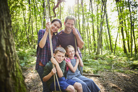 Porträt lächelnde Familie an Seilschaukel im Wald, lizenzfreies Stockfoto