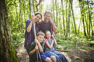 Portrait smiling family at rope swing in woods - CAIF09091
