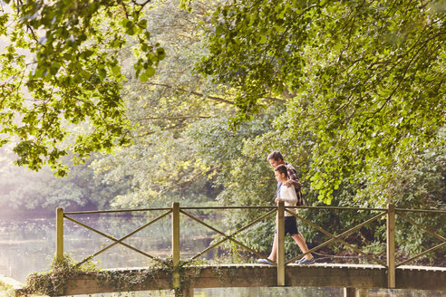 Vater und Sohn beim Überqueren einer Fußgängerbrücke in einem Park mit Bäumen - CAIF09095