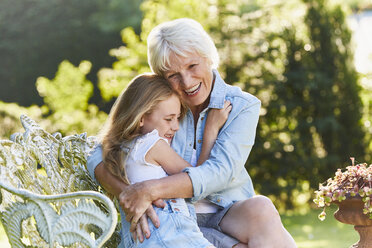 Grandmother and granddaughter hugging on garden bench - CAIF09105