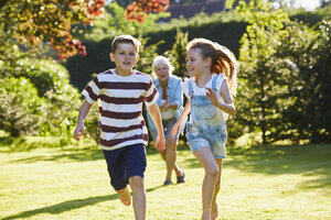 Bruder und Schwester laufen im sonnigen Garten - CAIF09108