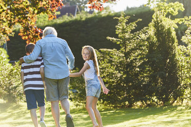 Portrait smiling girl walking with grandmother and brother in garden - CAIF09114