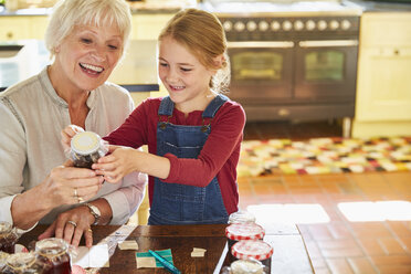 Grandmother and granddaughter labeling canning jars in kitchen - CAIF09116