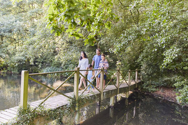 Family crossing footbridge in park with trees - CAIF09121