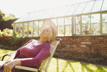 Sorglose ältere Frau entspannt sich vor einem sonnigen Gewächshaus - CAIF09123