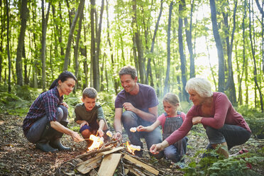 Multi-generation family roasting marshmallows at campfire in forest - CAIF09127