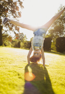 Mädchen macht Handstand im sonnigen Garten - CAIF09150