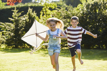 Bruder und Schwester laufen mit Drachen im sonnigen Garten - CAIF09178