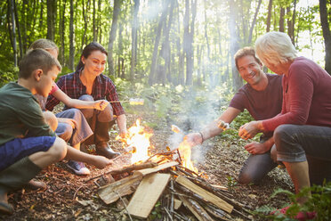 Multi-generation family roasting marshmallows at campfire in forest - CAIF09179