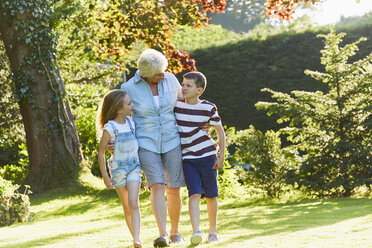 Großmutter und Enkelkinder beim Spaziergang im sonnigen Garten - CAIF09180