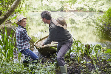 Vater und Sohn ziehen ein Boot auf einem Teich ans Ufer - CAIF09183