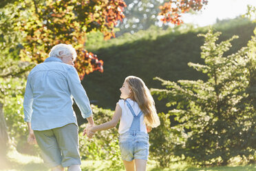 Grandmother and granddaughter holding hands and walking in sunny garden - CAIF09185