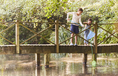 Bruder und Schwester fischen mit Netzen am Steg über den Teich - CAIF09189