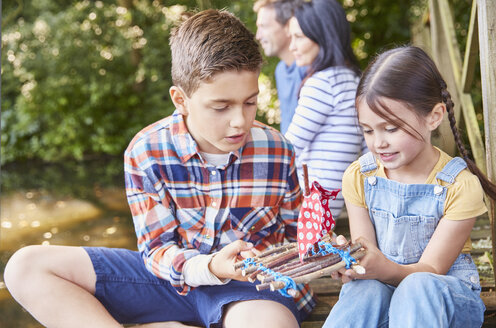 Bruder und Schwester bauen ein Spielzeugfloß aus Holz zusammen - CAIF09190