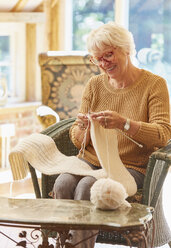 Smiling senior woman knitting scarf - CAIF09192