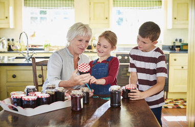 Grandmother canning jam with grandchildren in kitchen - CAIF09198