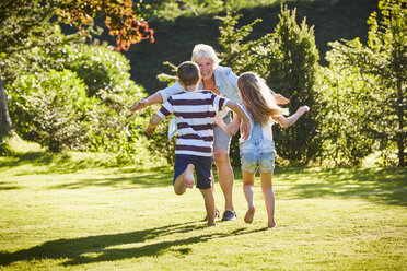 Grandchildren running to grandmother in sunny garden - CAIF09199