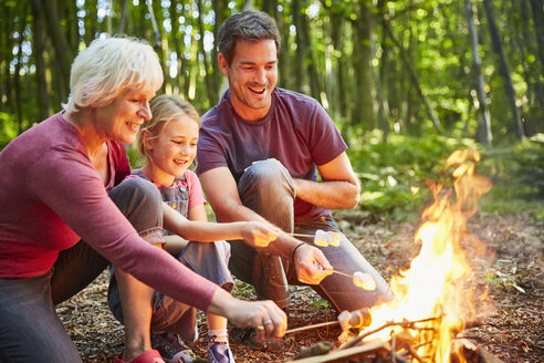 Mehrgenerationenfamilie röstet Marshmallows am Lagerfeuer im Wald - CAIF09207