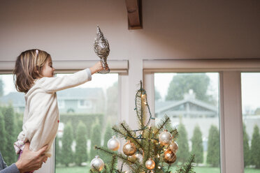 Toddler girl putting star on Christmas tree - CAIF09221