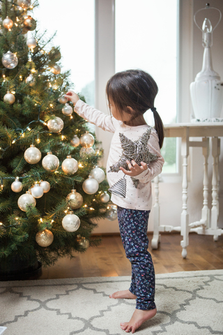 Mädchen im Kleinkindalter schmückt den Weihnachtsbaum, lizenzfreies Stockfoto