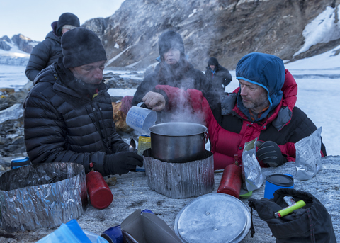 Grönland, Sermersooq, Kulusuk, Schweizerland Alpen, Gruppe von Menschen, die eine Pause machen und Wasser kochen, lizenzfreies Stockfoto