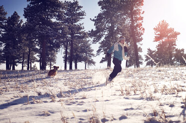 Playful woman with dog running on snow covered field - CAVF04124