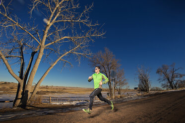 Mann joggt auf einem Feld gegen einen klaren blauen Himmel - CAVF04130