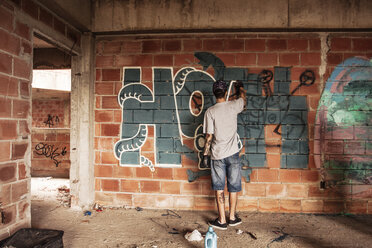 Rückansicht eines Mannes, der Graffiti auf eine Backsteinmauer sprüht - CAVF04146