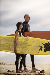 Seitenansicht eines älteren Paares mit Surfbrettern, das am Strand steht - CAVF04299