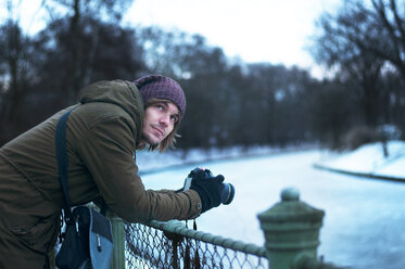 Man holding camera while leaning on railing - CAVF04324