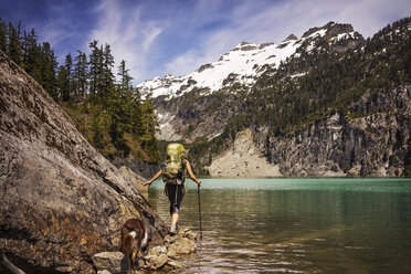 Rear view of woman with dog walking by lake - CAVF04373