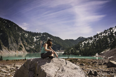 Side view of woman sitting on rock against mountain - CAVF04380