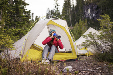 Woman drinking water while sitting at tent - CAVF04397