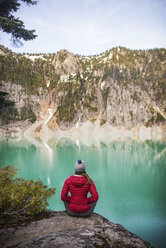 Rear view of woman sitting on mountain against lake - CAVF04403