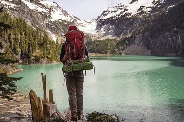 Rear view of man with backpack standing on mountain against lake - CAVF04410