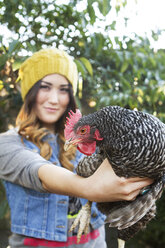 Porträt einer glücklichen Frau, die ein Huhn auf einem Bauernhof hält - CAVF04420