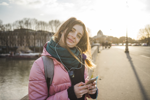 Paris, France, portrait of smiling young woman listening music with earphones and smartphone stock photo