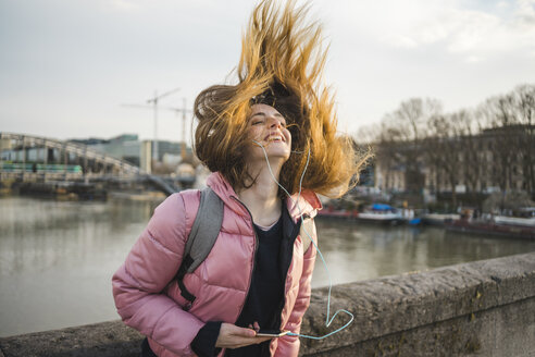 Paris, France, happy young woman listening music with earphones and smartphone tossing her hair - AFVF00288