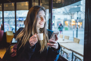 Paris, Frankreich, Porträt einer lächelnden jungen Frau mit Smartphone, die in einem Café Espresso trinkt - AFVF00292