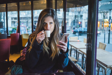 Paris, Frankreich, Porträt einer jungen Frau mit Smartphone, die in einem Café Espresso trinkt - AFVF00293