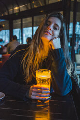 Paris, France, portrait of smiling young woman with glass of beer in a pub in the evening - AFVF00294