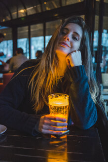 Paris, Frankreich, Porträt einer lächelnden jungen Frau mit einem Glas Bier in einer Kneipe am Abend - AFVF00294