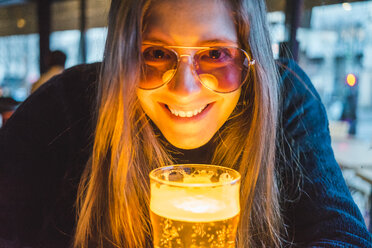 Paris, Frankreich, Porträt einer glücklichen jungen Frau mit einem Glas Bier in einer Kneipe am Abend - AFVF00295