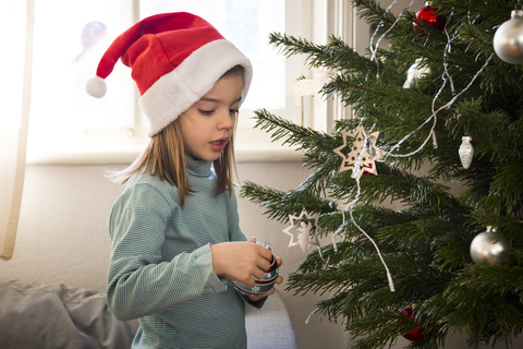 Kleines Mädchen mit Weihnachtsmütze beim Schmücken des Weihnachtsbaums, lizenzfreies Stockfoto