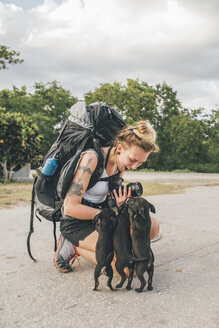 Kuba, junge Frau mit Rucksack streichelt junge Hunde, lachend - GUSF00536