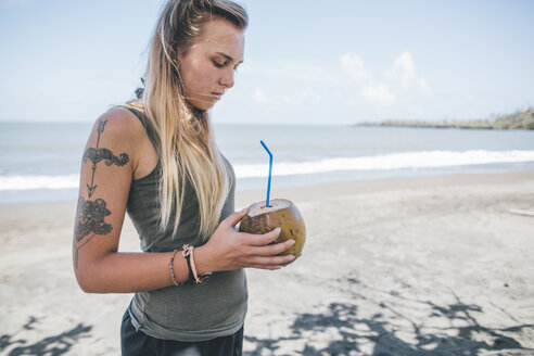 Kuba, Junge Frau mit Tätowierung am Playa de Miel trinkt Kokosnusswasser - GUSF00555