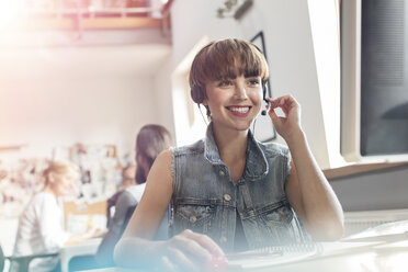 Lächelnder Design-Profi, der ein Headset mit Mikrofon im Büro benutzt - CAIF09243