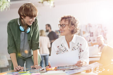 Lächelnde weibliche Design-Profis bei der Überprüfung von Korrekturabzügen im Büro - CAIF09255